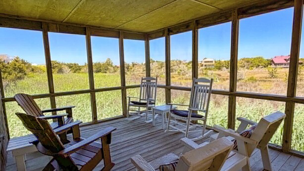 Eine überdachte Veranda mit Holzboden, mehreren Adirondack-Stühlen und Blick auf ein grünes Feld.