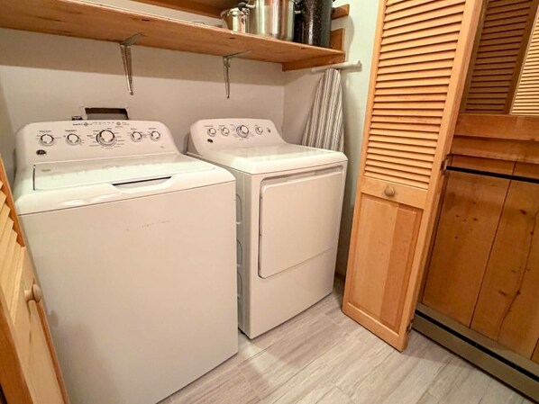 A laundry room with two white washing machines, wooden cabinets, and a wooden door. - Ford Cottage: Beautiful marsh views with a large screened porch. (Ocracoke)