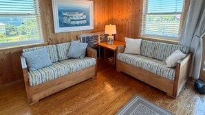 Ein Interieur einer Holzhütte mit Holzwänden, zwei Sofas mit gestreiften Kissen, einem Tisch mit einer Lampe und einem gerahmten Bild eines Bootes.