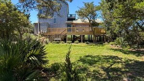 Ein zweistöckiges Holzhaus mit einer Terrasse, umgeben von üppiger Vegetation.