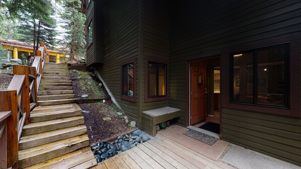 A wooden staircase leading to a house with a porch, a door, and a window.