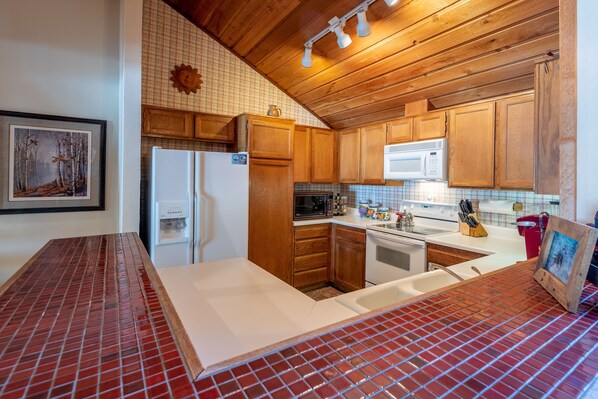 A kitchen with wooden cabinets, a white refrigerator, a microwave, and a tiled backsplash. - Sunburst Condo 2749 - Elkhorn Sunburst 2BR Loft Near Sun Valley (Elkhorn)