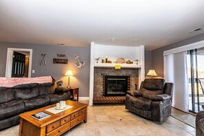 A living room with a fireplace, leather sofas, a wooden coffee table, and a door with a sign. - Knolls 1111 - Three Bedroom Apartment, Sleeps 8 (Osage Beach)
