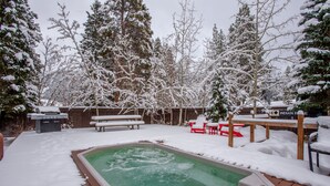 Ein Garten mit einem Whirlpool, umgeben von schneebedeckten Bäumen und einer Holzterrasse.