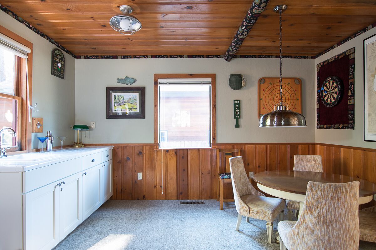 A kitchen with wooden paneling, a dining table with chairs, a window, and a dartboard on the wall.