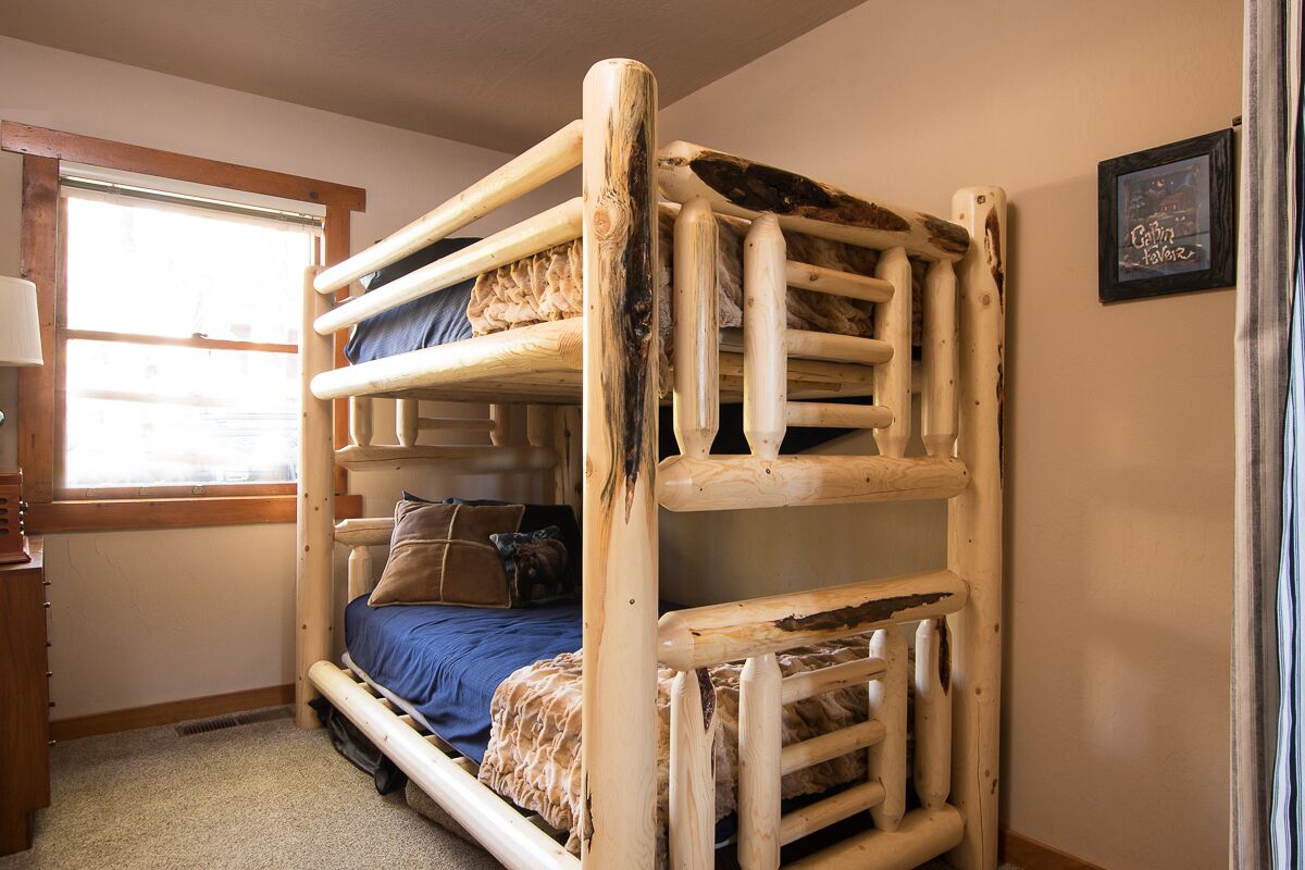 Een stapelbed met houten frame, een raam met zonwering, een nachtkastje en een lijst met een afbeelding aan de muur.