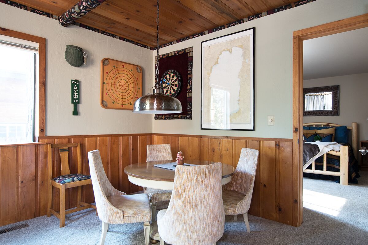 A dining area with a round table, four chairs, a hanging lamp, a dartboard, and a framed picture on the wall.