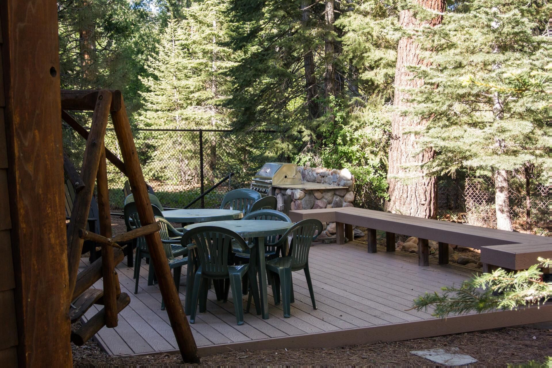 Une terrasse extérieure avec un barbecue en pierre, des chaises en plastique vert et une échelle en bois.