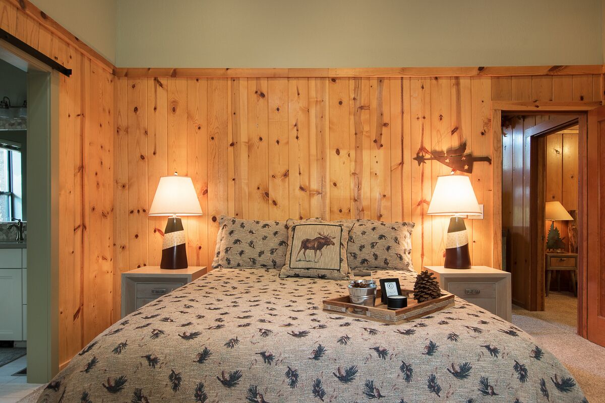 Een slaapkamer met houten lambrisering, een bed met een beddegoed met dessin, twee bedlampen en een nachtkastje met een dienblad.