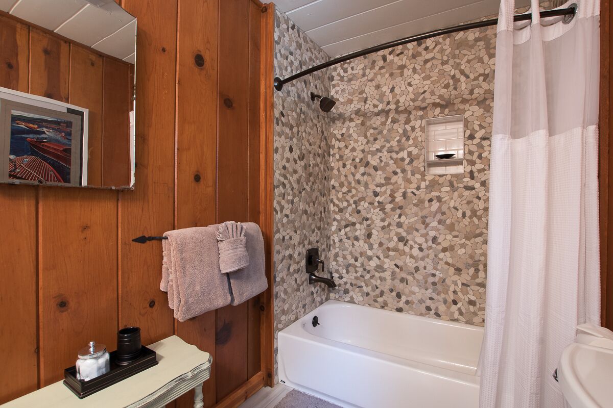 A bathroom with a wooden wall, a bathtub, a shower, and a sink with a mirror.