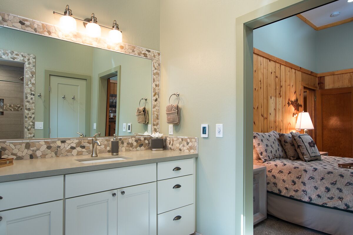 A bathroom with a stone mosaic backsplash, a large mirror, and a vanity with a sink and drawers.