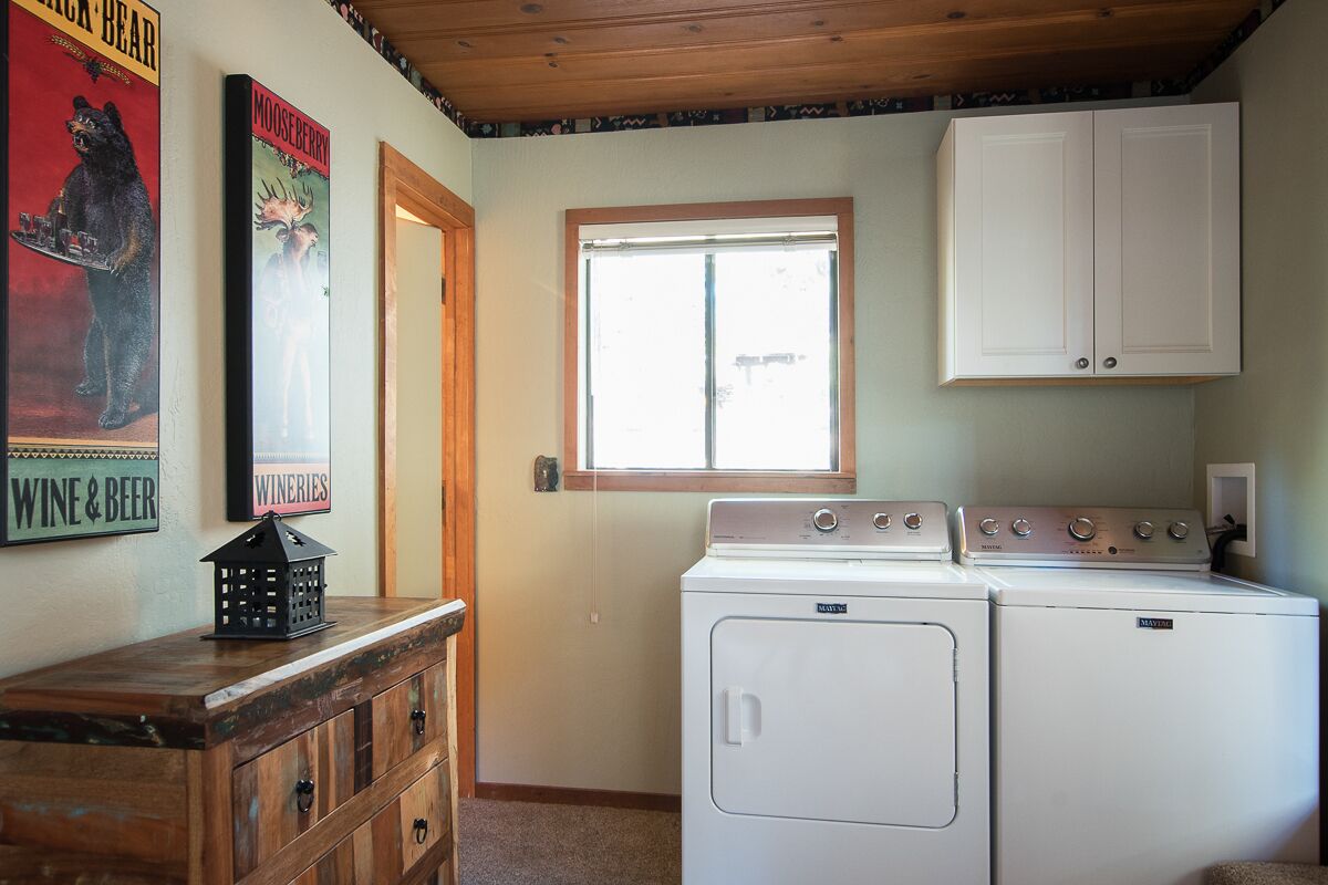 A laundry area with a washer and dryer, wooden cabinets, and a window.