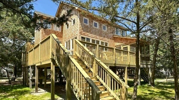 Una baita di legno con veranda e scale, immersa tra gli alberi.