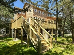 Una cabaña de madera con terraza y escaleras, rodeada de árboles.