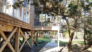 Un pontile in legno conduce a una baita con ampie finestre e un balcone, immersa nel verde.