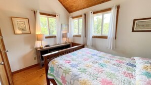 Una camera da letto con soffitto in legno, un letto con copriletto colorato, due lampade da comodino, un comodino e una finestra con tende.