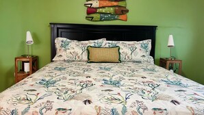 A bed with a floral bedspread, a decorative pillow, and a wall art piece above it.