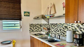 A kitchen with wooden cabinets, a tiled backsplash, a small shelf with a sailboat model, and a window with blinds.