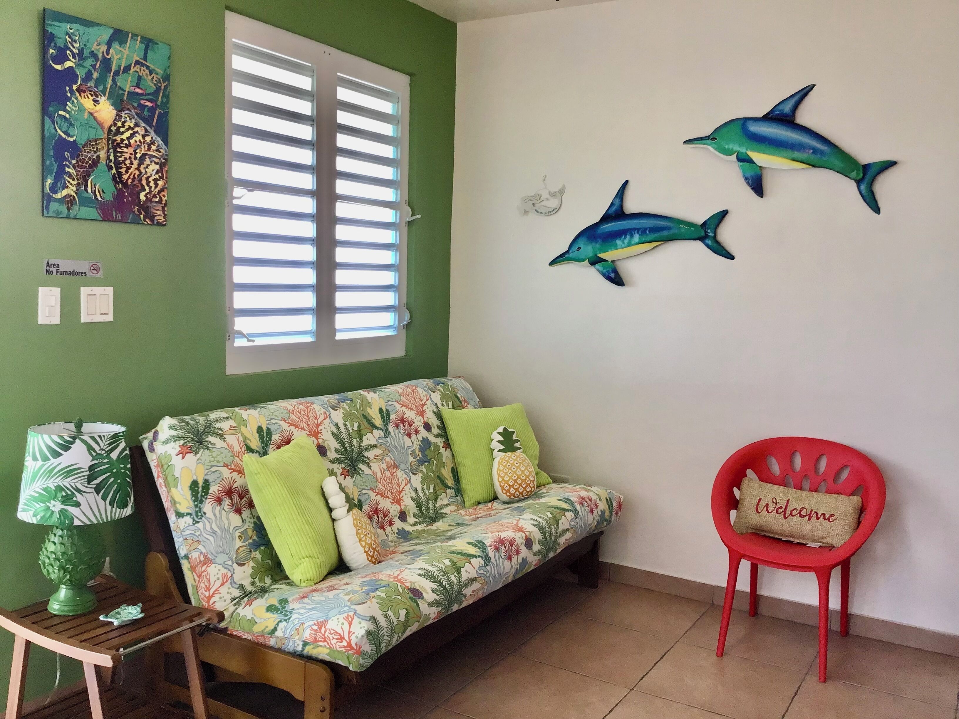 Ein Zimmer mit grüner Wand, einem blumigen Sofa, einem roten Sessel und Wandbildern von Delfinen.