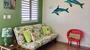 A room with a green wall, a floral sofa, a red chair, and wall art of dolphins.