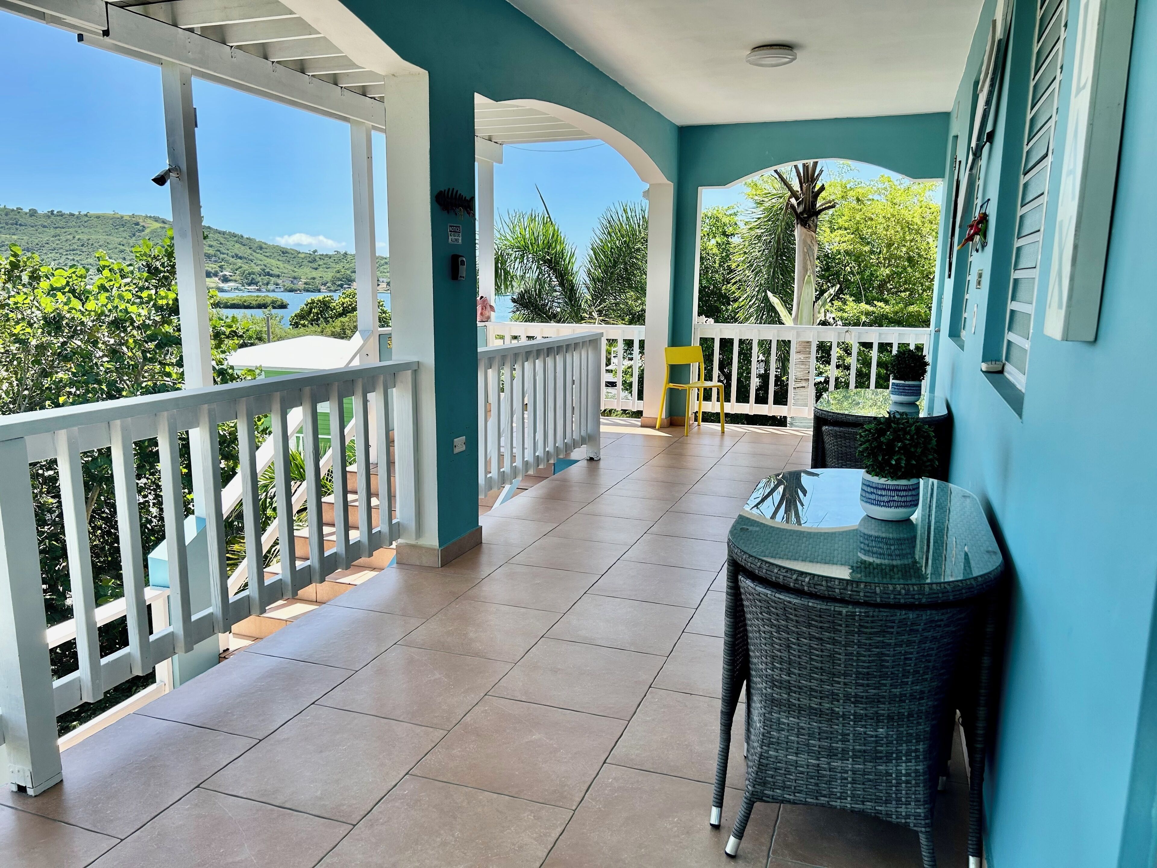 A covered balcony with a view of a green landscape and a body of water.