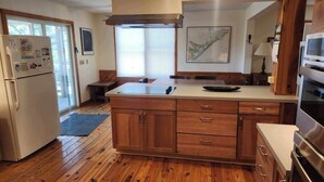 Una cocina con armarios de madera, un refrigerador de acero inoxidable, horno empotrado y un ventanal con persianas.