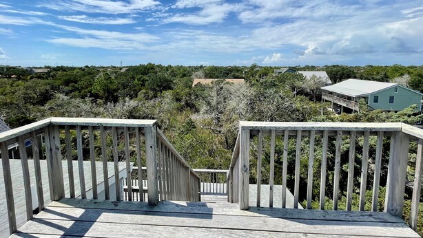 Terraza de madera con vista a una casa verde y árboles circundantes.