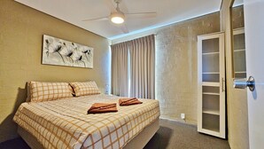 Un dormitorio con cama, ventilador de techo, un cuadro y una puerta con panel de vidrio.