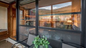 A room with a large window, a plant on a table, and a view of a dining area with chairs and a lamp. - Ski-in Ski-Out free wifi, underground parking, middle of Center Village. (Copper Mountain)