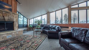 A spacious living room with a stone fireplace, leather sofas, and large windows offering a view of snow-covered trees. - Ski-in Ski-Out free wifi, underground parking, middle of Center Village. (Copper Mountain)
