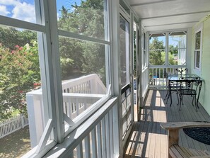 Une véranda avec une terrasse en bois, une table et des chaises, et une vue sur un jardin agrémenté d’arbres et de fleurs.