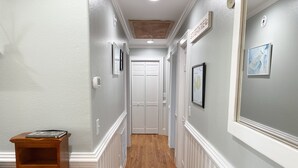 A hallway with white wainscoting, a wooden floor, and framed artwork on the walls. - Sun Kissed: Cheerfully decorated dog friendly cottage. (Ocracoke)