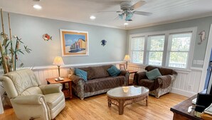 A living room with a beige armchair, two brown sofas, a round wicker coffee table, and a ceiling fan. - Sun Kissed: Cheerfully decorated dog friendly cottage. (Ocracoke)