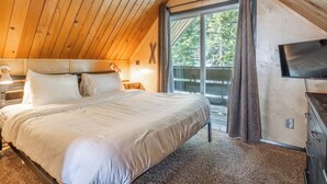Makuuhuoneessa on suuri sänky, puinen katto ja seinälle asennettu televisio.
