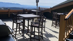 Een terras buiten met tafels en stoelen, een lantaarnpaal en uitzicht op bergen.