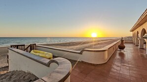 Une vue sur la plage au coucher du soleil, avec un kayak jaune et un bâtiment doté d’arcades.