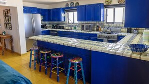 Une cuisine avec des meubles de rangement bleus, un îlot central doté de tabourets, un réfrigérateur, un four à micro-ondes et une cuisinière.