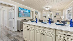 Una cocina amplia con una isla grande, armarios blancos y un televisor de pantalla plana montado sobre la isla.