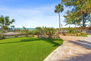 A well-maintained garden with a lawn, palm trees, and a view of the ocean.