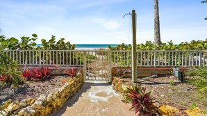 Un sendero que lleva a una playa con una cerca blanca y plantas tropicales.