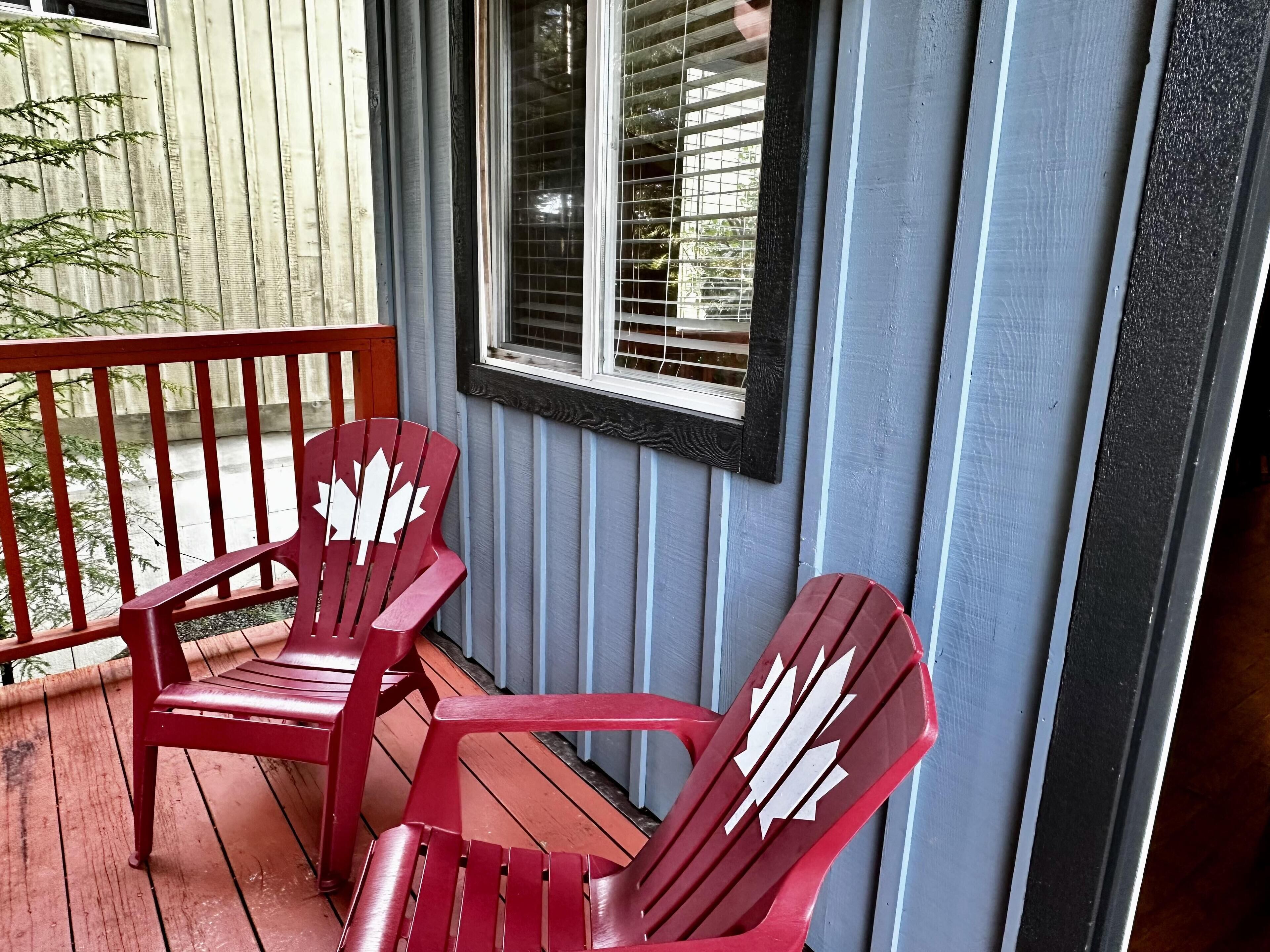 Une véranda avec deux fauteuils Adirondack rouges et une fenêtre avec des stores.