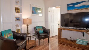 Un salón con dos sillones de cuero, una mesa de centro de vidrio, un televisor sobre un mueble de madera, y una pared decorada con cuadros y un cuadro.