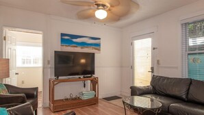 Una sala de estar con televisión, sofá de cuero y ventilador de techo.