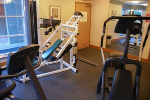 Un gimnasio con equipo de ejercicio, una cinta de correr y un espejo que refleja el espacio.