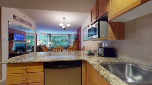 Una cocina con encimeras de granito, armarios de madera, lavavajillas, microondas y tostadora.