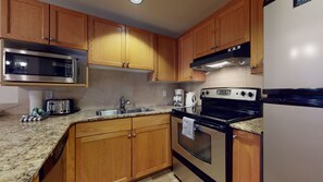 A kitchen with wooden cabinets, a stainless steel microwave, a gas stove, and a refrigerator. - Woodrun Lodge - True Ski In/Ski Out, Pool, Hot Tub, Perfect for Families (Whistler)