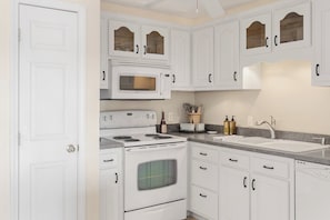 A kitchen with white cabinetry, a microwave, stove, oven, and a sink.