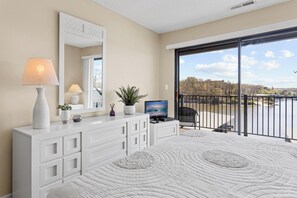 A bedroom with a large window, a TV, and a balcony with a view of a body of water.