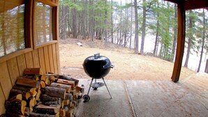 Un espace extérieur abrité, équipé d’un barbecue et d’une pile de bois de chauffage.