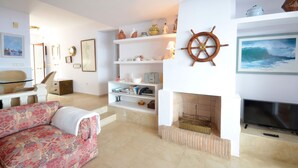 A living room with a sofa, shelves with decorative items, a fireplace, and a television. - Holiday rental apartment with swimming pool in Begur, Aiguafreda (Begur)